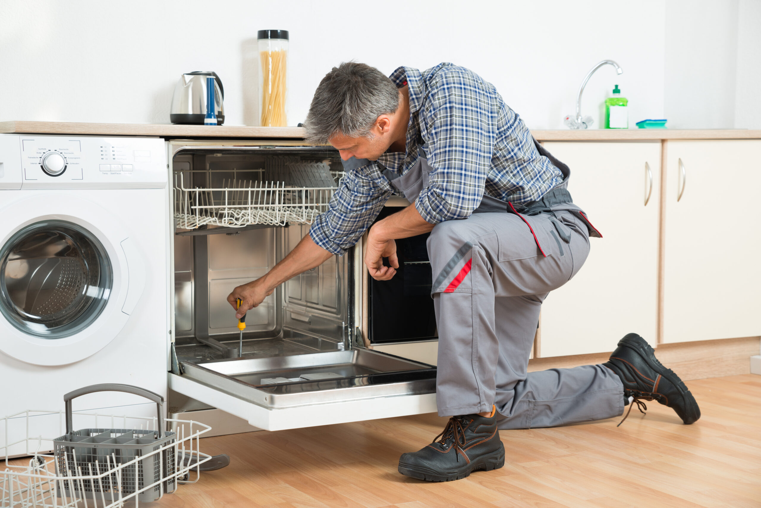 Full length of repairman repairing dishwasher with screwdriver in kitchen